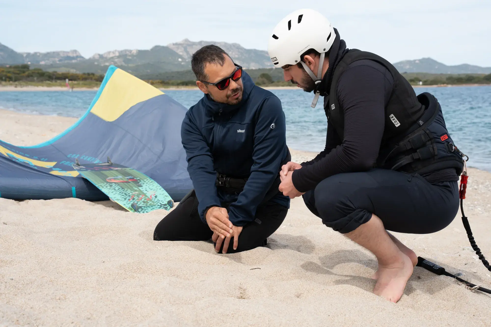 Istruttore che spiega le basi del kitesurf a un allievo principiante sulla spiaggia delle Saline, Olbia